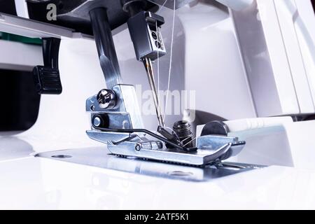 Piede premitore della macchina da cucire con ago e filo in primo piano. Particolare della macchina cucitrice. Il piede della macchina da cucire con un ago. Linea di produzione con Foto Stock