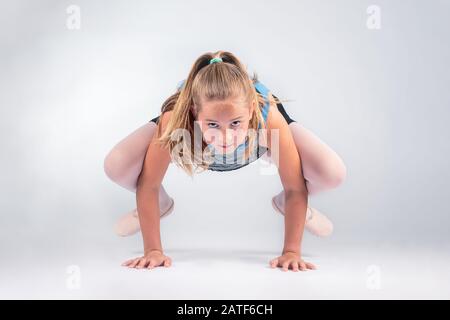 studio ritratto scatto di una giovane limber potente ragazza in abito da ballo equilibrio sulle sue mani, mentre guardando la fotocamera. isolato su sfondo grigio Foto Stock