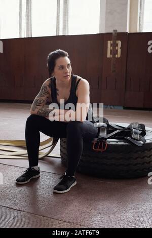 Giovane atleta caucasico femminile con tatuaggi seduti sul pneumatico Foto Stock