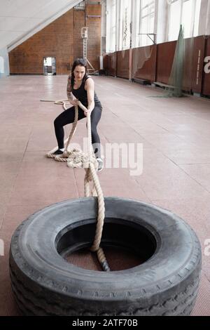 Giovane atleta caucasico femminile che tira pneumatici pesanti con corda da battaglia Foto Stock