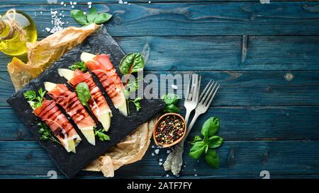 Prosciutto con melone su un piatto di pietra. Antipasto tradizionale italiano. Vista dall'alto. Spazio libero di copia. Foto Stock