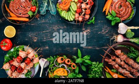 Assortimento di carne di barbecue al forno. Salsicce, spiedini, verdure fresche. Pomodori, cipolle, aglio. Su uno sfondo di legno. Spazio di copia. Foto Stock