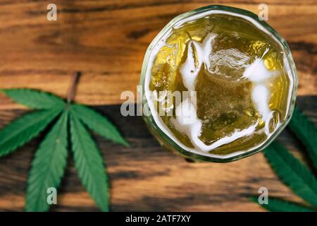 Marijuana ghiacciata cannabis infuso THC bere in un cristallo trasparente con foglie di erbaccia su uno sfondo di legno scuro. Bevande medicinali CBD Foto Stock