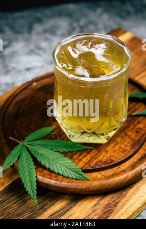 Marijuana ghiacciata cannabis infuso THC bere in un cristallo trasparente con foglie di erbaccia su uno sfondo di legno scuro. Bevande medicinali CBD Foto Stock