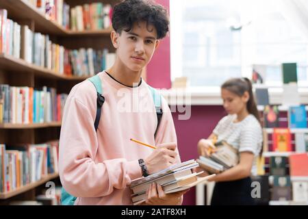 Geniale adolescente in felpa che ti guarda in piedi da scaffale Foto Stock