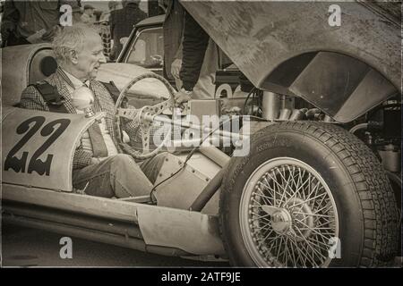 Un Signore siede in una vettura sportiva d'epoca con il cofano sollevato al Revival Goodwood Foto Stock