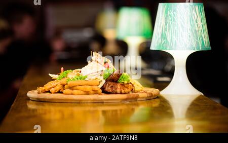 Snack per la birra. Tavola di legno con un sacco di patatine fritte bastoncini di pesce burrito e bistecca di carne con insalata mista. Pub menu snack. Ad alto contenuto calorico snack per il gruppo amici. Gustosi spuntini deliziosi. Il cibo del ristorante. Foto Stock