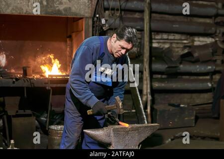 l'uomo maturo fabbro al lavoro forge un pezzo rosso-caldo di metallo Foto Stock