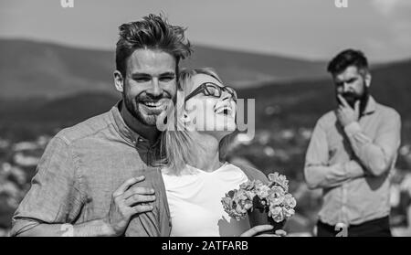 Gli amanti abbracci outdoor flirt romanticismo relazioni. Coppia romantica data amanti fiori bouquet. Concetto di infedeltà. Coppia nell'amore che datano mentre l'uomo geloso bearded che guarda la moglie che lo bardisce con l'amante. Foto Stock