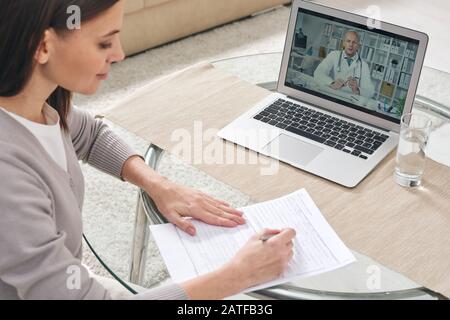 Giovane donna che compila il modulo di assicurazione sanitaria e guarda il video online Foto Stock