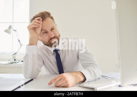 Un uomo d'affari serio e impegnato legge i documenti di lavoro seduti a un tavolo con un computer in ufficio. Foto Stock