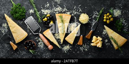 Formaggio duro con olive e coltello formaggio su fondo di pietra nera. Parmigiano. Vista dall'alto. Spazio libero per il testo. Foto Stock