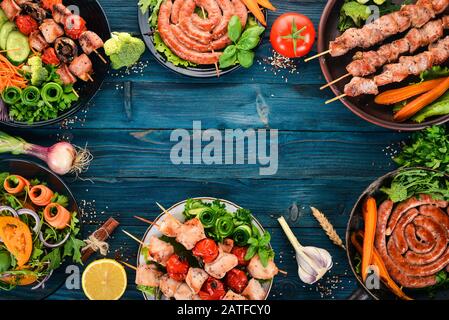 Una serie di carni e verdure fresche. Barbecue, salsicce, bistecche. Su uno sfondo di legno blu. Spazio di copia. Foto Stock