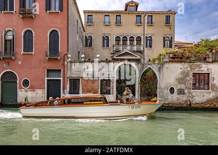 Un taxi d'acqua di Venezia parla sul suo telefonino che naviga lungo il Rio dei Medici un canale nel quartiere Cannaregio di Venezia Foto Stock