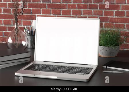 Area di lavoro con monitor per laptop vuoto, schermo bianco, modellato sulla scrivania scura vicino a una parete di mattoni rossi Foto Stock