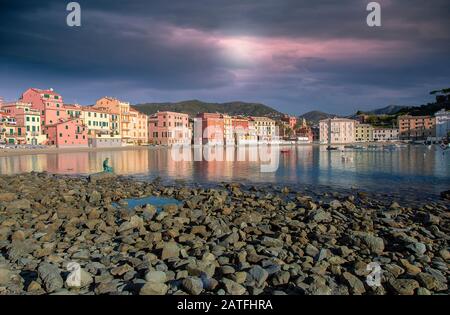 Vista dalla baia alle colorate case sul lungomare di Sestri Levante sulla Riviera Italiana, con una spiaggia rocciosa in primo piano e il colorato clou rosa Foto Stock