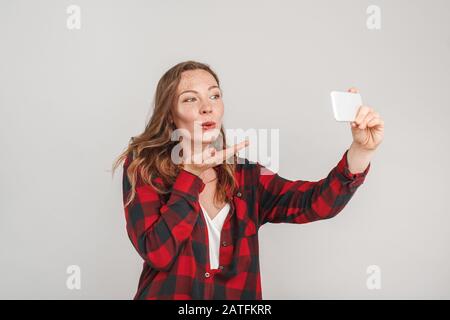 Stile Libero. Giovane donna con i temerari isolati sul grigio scattare foto selfie invio bacio alla fotocamera giocoso Foto Stock