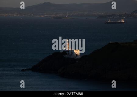 Il faro di Baily, Howth. co. Dublino, Faro di Baily sulle scogliere di Howth, Vista del faro di Baily dalla scogliera con la nave da carico sullo sfondo Foto Stock