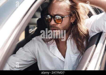 Giovane adulto seduto in auto con occhiali da sole Foto Stock