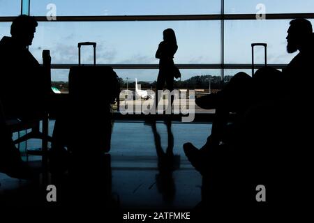 Sagoma dei passeggeri delle compagnie aeree in una sala d'aeroporto all'ampia finestra di osservazione che guarda un aereo che vola contro un tramonto surreale. Dublino Foto Stock