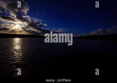 Il tardo sole sguance attraverso le nuvole sopra il campo di fattoria allagato Foto Stock