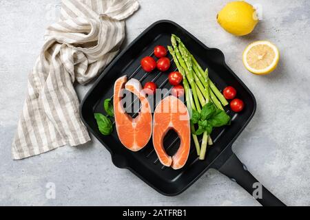 Bistecche Di Salmone, Asparagi E Verdure Su Una Griglia. Bistecca Di Pesce Crudo E Verdure. Cottura Foto Stock