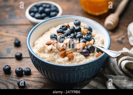 Porridge di farina d'avena con mirtilli, mandorle in ciotola su sfondo di tavolo di legno. Cibo sano per la colazione Foto Stock