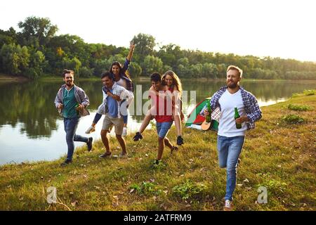 Gli amici hanno divertimento che corre lungo il lago su un picnic. Foto Stock