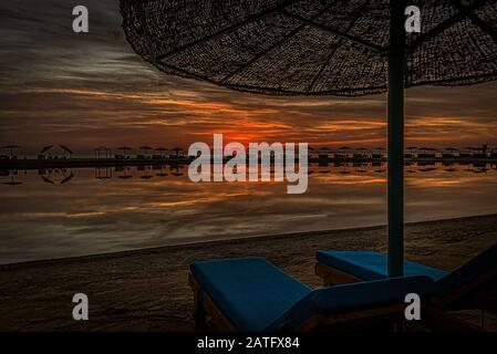 Due sedie a sdraio blu e un ombrellone in spiaggia nel mare rosso al tramonto, El Gouna, Egitto, 16 gennaio 2020 Foto Stock