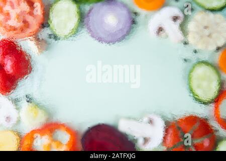 Verdure assortite affettate su sfondo verde disposte in una cornice con spazio copia al centro. Immagine fuori fuoco, texture gocce d'acqua Foto Stock