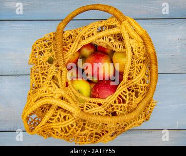 Mele fresche in un sacchetto di corde in tessuto prodotto riutilizzabile e ecologico. Su uno sfondo di legno blu. Foto Stock
