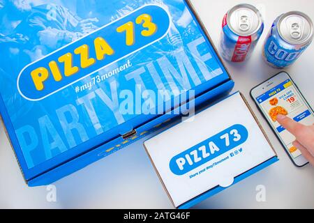 Una Pizza 73 Pizza box con ali e una Dieta coke con Nostea pop e persona che usa la Pizza 73 app Foto Stock