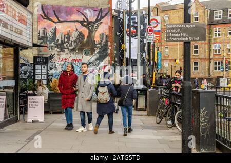 Una vista lungo il marciapiede lungo City Road a Londra, Regno Unito. Sullo sfondo, la colorata Street art è dipinta su un muro di mattoni Foto Stock