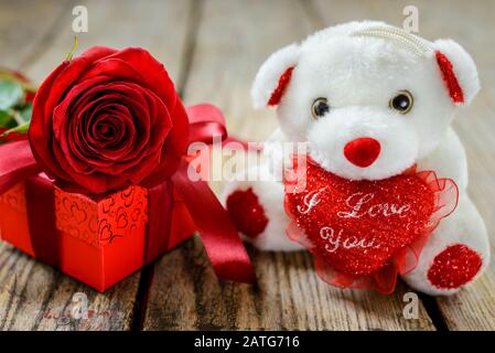 San Valentino e il concetto di Festa della Donna. Orso peluche bianco giocattolo, scatola regalo e rosa rossa su tavolo di legno. Messa a fuoco selettiva. Foto Stock