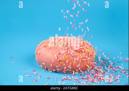 Spruzzate che cadono dall'alto su Una Gustosa ciambella rosa di fragole. Delizioso dessert su sfondo blu. Foto Stock
