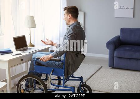 Giovane handicappato in sedia a rotelle che usa il laptop a casa Foto Stock