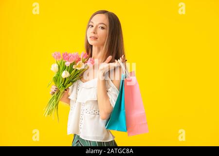 Bella giovane donna con shopping borse e fiori su sfondo a colori. Celebrazione della Giornata Internazionale della Donna Foto Stock