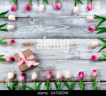 Happy Mothers Day Holiday Concept con scatola marrone regalo e bordo di tulipani rosa su sfondo bianco rustico in legno Foto Stock