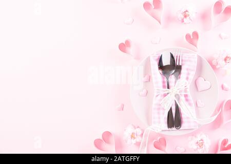 Cuori di carta rosa con set da tavolo con set di argenti e cucchiaio su sfondo di carta pastello rosa chiaro. Amore e concetto di San Valentino. Foto Stock