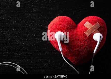 Fascia di pronto soccorso striscia di gesso imbottito cerotto medico incollato sul cuore rosso con auricolare ascoltare musica su sfondo di legno. Cuore spezzato, Amore e Val Foto Stock