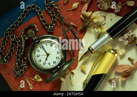 Orologio tascabile vintage e penna in ottone su vecchio libro. Alle 8 del mattino. Primo piano e vista dall'alto. Educazione e concetto di stile vintage. Foto Stock