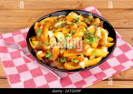 Ciotola di tradizionale poutine canadese su uno sfondo di legno Foto Stock