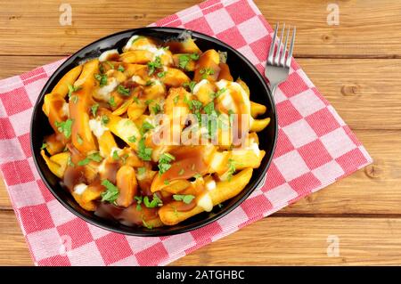 Ciotola di tradizionale poutine canadese su uno sfondo di legno Foto Stock