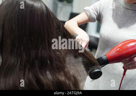 Cromwell, CT / USA - 27 dicembre 2019: Primo piano di un parrucchiere asiatico che raddrizza i capelli di una mecenate femminile Foto Stock