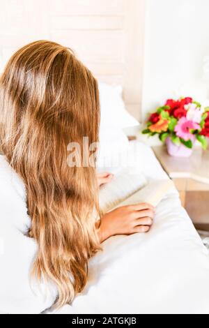 Ragazza rilassante nella sua camera d'albergo: Leggere un libro. Vacanza, relax, self time e concetti di fuga. Verticale Foto Stock