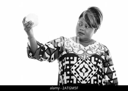 Studio shot di donna africana in sovrappeso guardando sotto la banca piggy Foto Stock