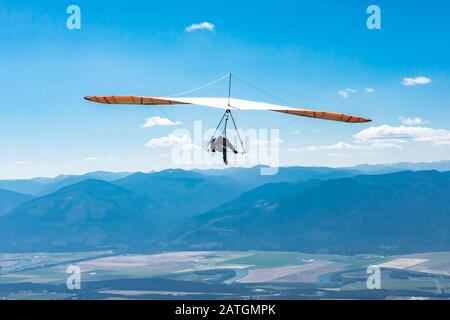 Deltaplano uomo volare in chiaro giorno di sole. Volo sulle montagne della valle di Kootenay, Creston, British Columbia, Canada. Scatto lungo Foto Stock