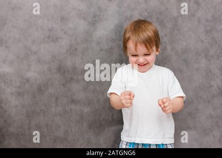 Ragazzo arrabbiato sta mostrando i suoi muscoli del braccio. Ritratto del ragazzo dell'aspetto europeo su sfondo grigio. Concetto di problemi parenting Foto Stock