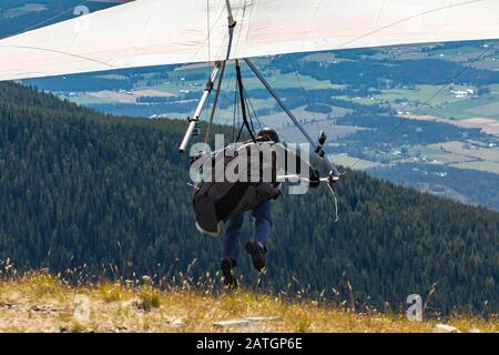 Deltaplano professionista che corre e decenti. Vista dalla parte posteriore. Volo di deltaplano in azione. Volare dalla cima della montagna Foto Stock