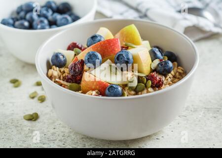 Bircher muesli o farinata d'avena da notte con mela, banana e mirtilli in una ciotola grigia. Foto Stock